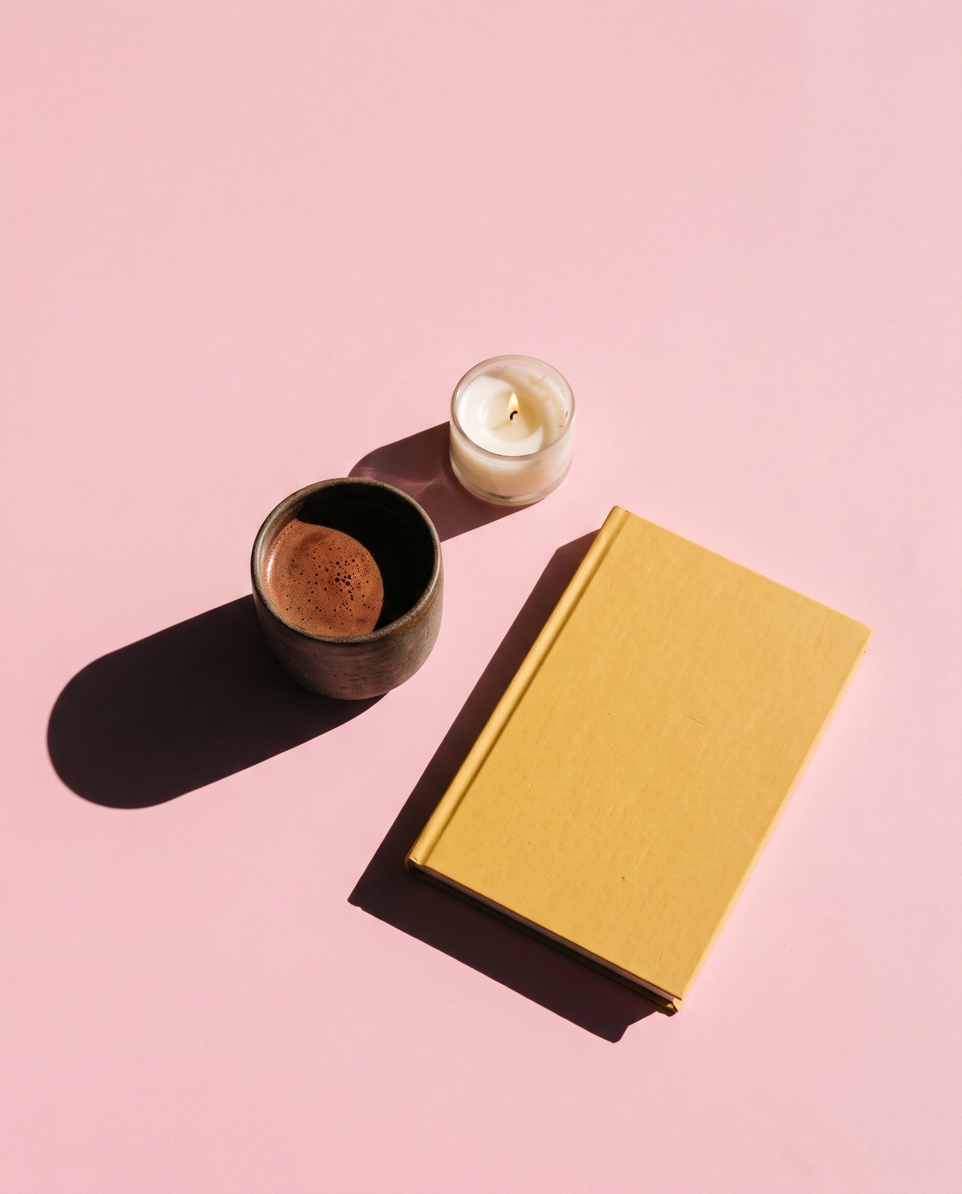A cup of cacao, a candle and a journal on a pink cloth